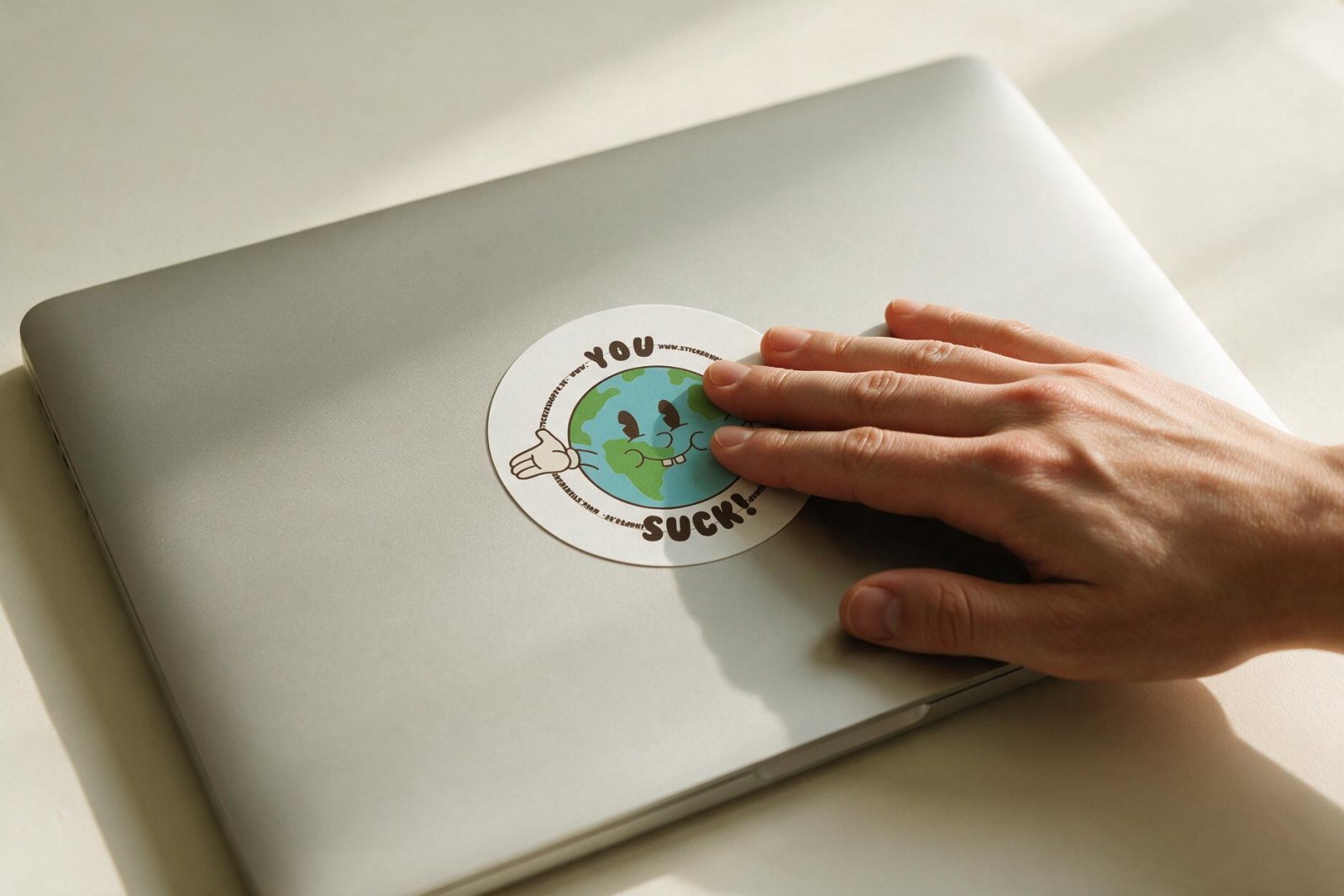 Eine Hand drückt den You-Suck-Sticker auf den Laptopdeckel